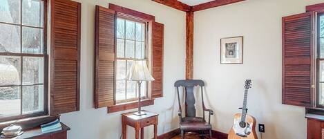 A room with wooden beams, a guitar, a chair, and a table with a lamp.