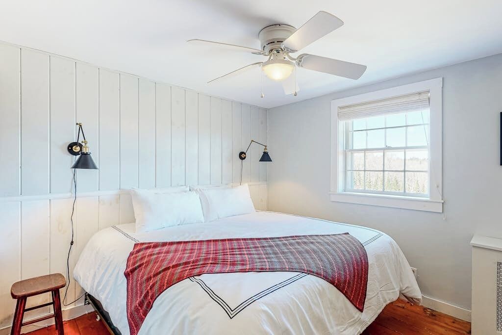 Une chambre à coucher avec un lit, un ventilateur de plafond, une fenêtre et une table de chevet.
