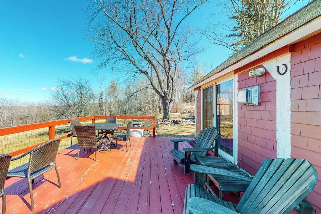Una terraza de madera con mobiliario exterior, un espacio cubierto con una mesa y sillas, y vistas del paisaje circundante.