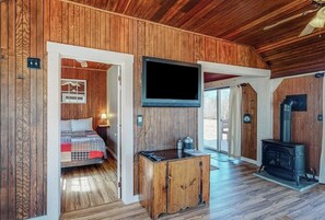 Ein Holzinnenraum mit einem Bett, einem Fernseher, einem Holzschrank und einem Kaminofen.