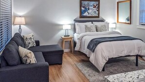 Ein Schlafzimmer mit einem Bett, Nachttischen, einem Sofa, einem Teppich und einem Fenster mit Jalousien.
