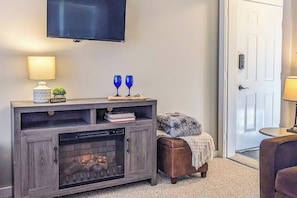 A living room with a fireplace, a television mounted on the wall, and a door to the right. - 6 Cozy Condos in the heart of Ludlow, fireplace, kitchenettes, shuttle nearby (Ludlow)