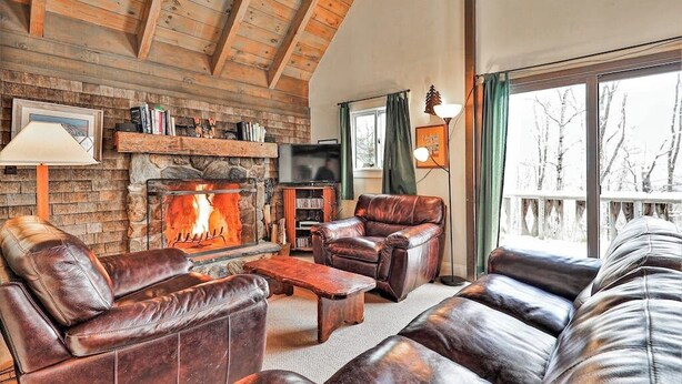 A cozy living room with leather furniture, a stone fireplace, and a large window.