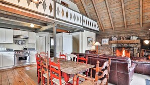 A rustic interior with a dining table, chairs, a fireplace, and a leather sofa.