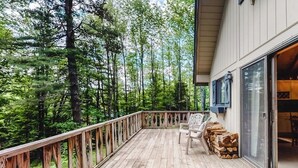 A wooden deck with a railing, a chair, and a stack of firewood.