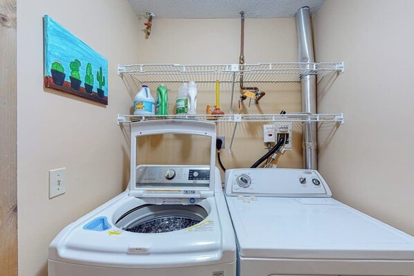 A laundry room with a washing machine, dryer, and shelves holding cleaning supplies.