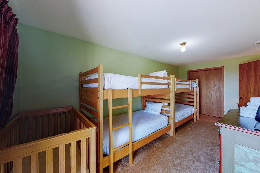 A room with bunk beds, a wooden crib, a cabinet, and a door.