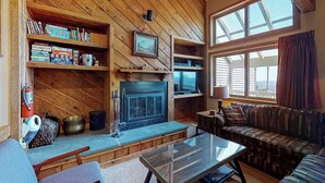 Ein gemütliches Wohnzimmer mit Kamin, Holzregalen, einer Couch und einem großen Fenster.