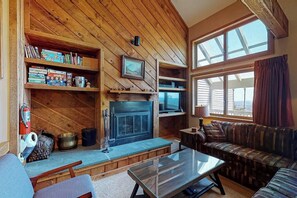 Ein gemütliches Wohnzimmer mit Kamin, Holzregalen, einer Couch und einem großen Fenster.