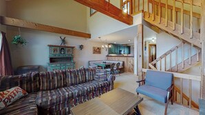 Ein geräumiger Wohnbereich mit einer Holztreppe, einem Sofa, einem Sessel und einer Küche im Hintergrund.