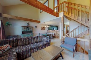 Ein geräumiger Wohnbereich mit einer Holztreppe, einem Sofa, einem Sessel und einer Küche im Hintergrund.