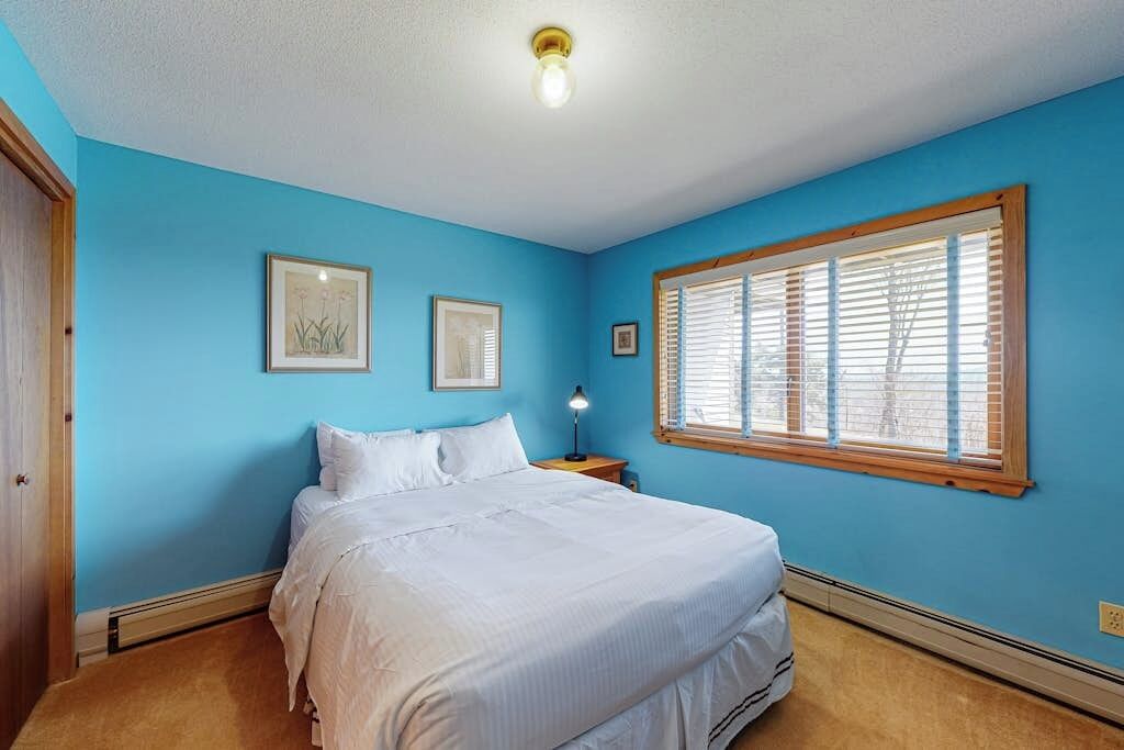 A bedroom with a bed, a nightstand, a lamp, and a window with blinds.
