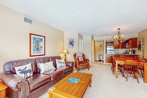 A living room with a brown leather sofa, a wooden coffee table, and a dining area with a wooden table and chairs. - Ski-in/out condo with mountain views, fireplace, pool, & hot tub (Ludlow)