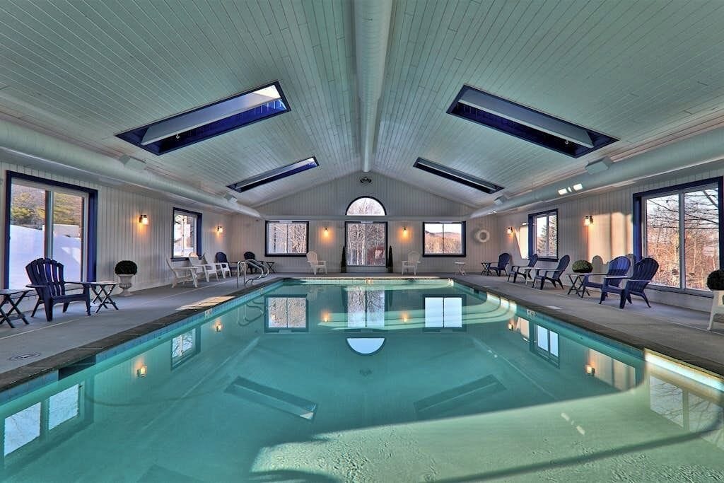 An indoor swimming pool with a high ceiling, skylights, and seating areas.