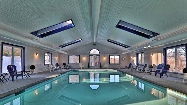 Une piscine intérieure dotée d’un haut plafond, de fenêtres de toit et d’espaces aménagés pour s’asseoir.