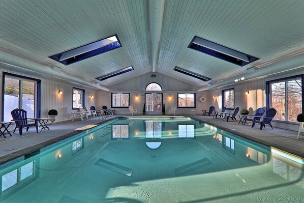 An indoor swimming pool with a high ceiling, skylights, and seating areas. - Ski-in/out condo with mountain views, fireplace, pool, & hot tub (Ludlow)
