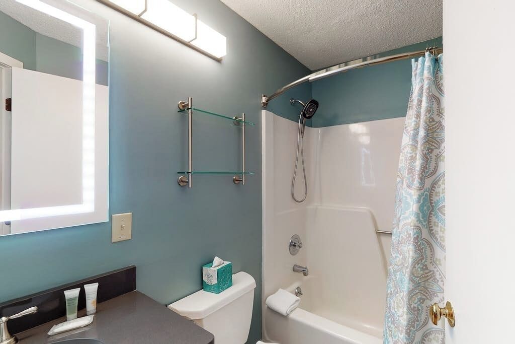 Ein Badezimmer mit Dusche, Toilette und Waschbecken, darüber ein Ablagebalken aus Glas.
