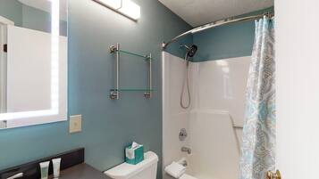 Ein Badezimmer mit Dusche, Toilette und Waschbecken, darüber ein Ablagebalken aus Glas.
