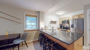 Una cocina moderna con una isla central, taburetes de bar, una mesa de comedor y un ventanal.