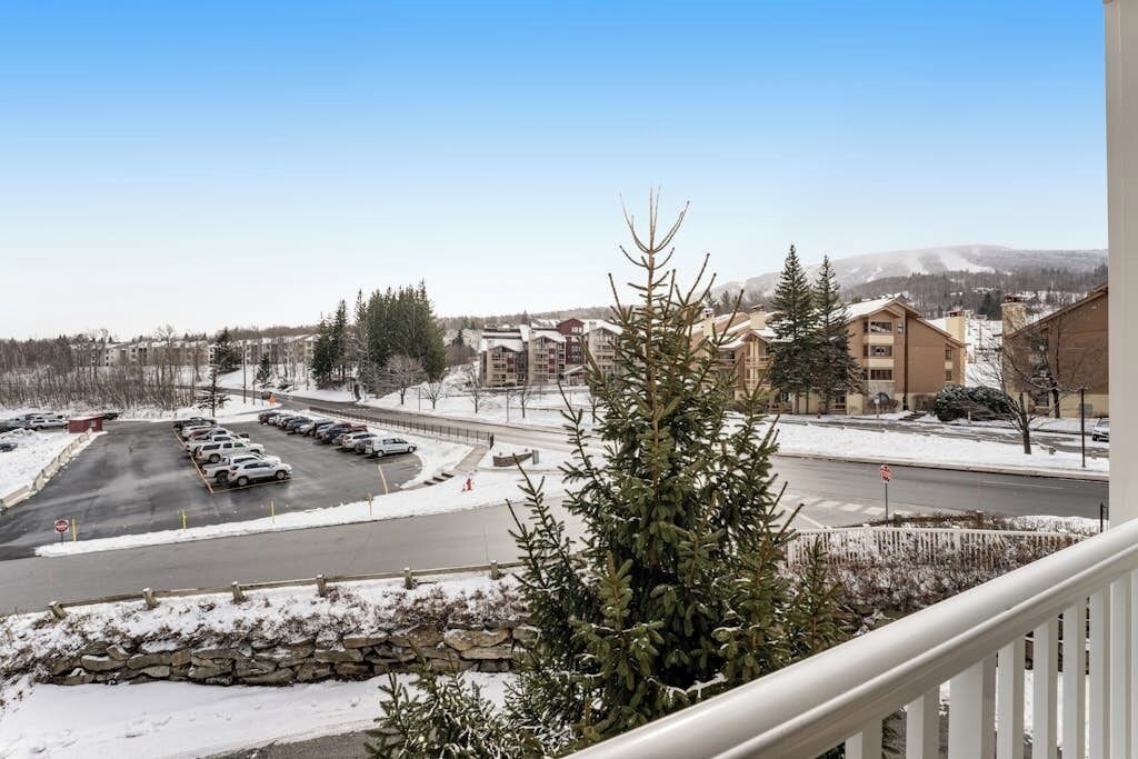 A view of a parking lot with several cars, a stone wall, and buildings in the background.