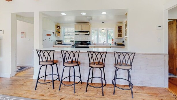 Een keuken met houten balken, een centraal eiland met barstoelen en uitzicht op aangrenzende kamers.