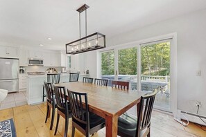A modern kitchen with white cabinets, a wooden dining table, and a large sliding glass door leading to a deck. - Peaceful mountain home near skiing, hiking, mtn biking & more (Jamaica)