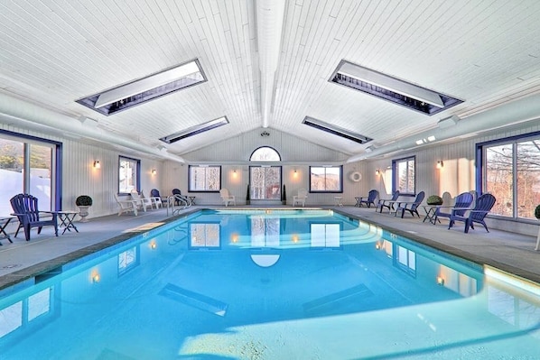 Ein großer, überdachter Schwimmbereich mit Deckenfenstern, Liegestühlen und großen Fenstern.