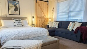 Une chambre à coucher avec un lit, un canapé, une porte en bois et une affiche accrochée au mur.