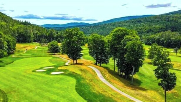 Un parcours de golf avec un sentier sinueux, des arbres et un paysage vallonné.