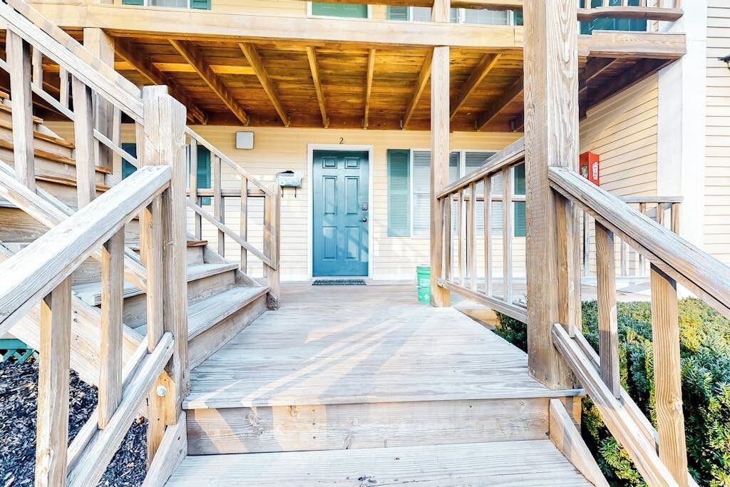 Una terraza de madera que conduce a un edificio con una puerta azul y el número 2 encima.