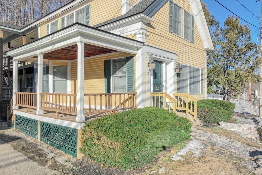 A two-story house with a covered porch, a small garden, and a stone pathway.