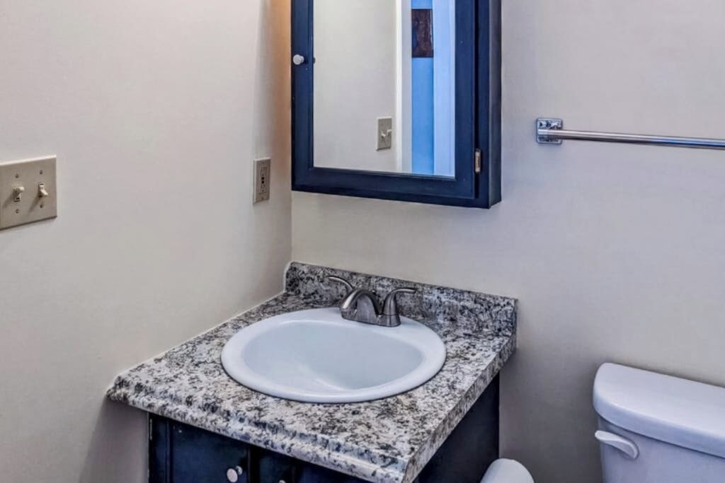 Une salle de bain avec un lavabo doté d’un plan de travail en granit, un miroir, un porte-serviettes et des toilettes.