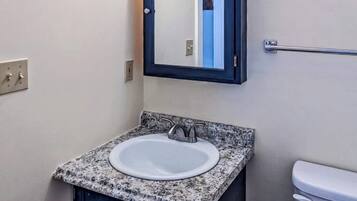 Une salle de bain avec un lavabo doté d’un plan de travail en granit, un miroir, un porte-serviettes et des toilettes.