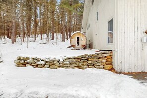 A rustic cabin with a stone wall entrance, surrounded by a snowy forest.