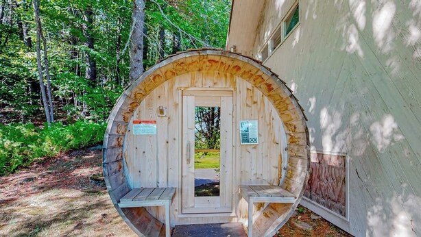 Eine rustikale Holzhütte mit Tür, Stufen und einer Bank, umgeben von Bäumen.