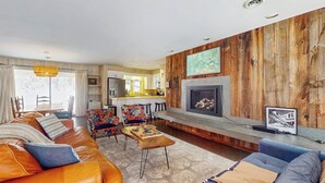 Ein Wohnzimmer mit einer Couch, Sesseln, einem Kamin und einer Küche im Hintergrund.