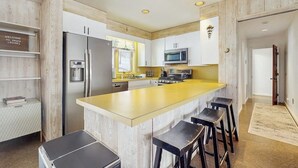 Eine moderne Küche mit einer zentralen Kochinsel, Barhocker, einem Kühlschrank, einer Mikrowelle und einer Wand mit Holzvertäfelung.