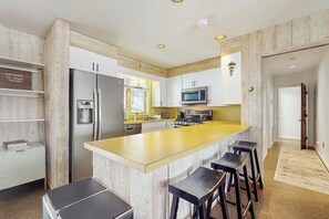A modern kitchen with a central island, bar stools, a refrigerator, microwave, and a wooden accent wall.