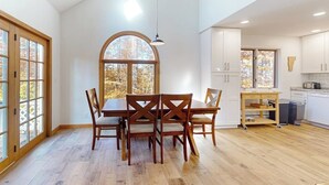 Uma sala de jantar ampla com uma mesa grande e cadeiras, uma cozinha com armários brancos e uma vista pela janela.