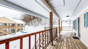 A covered wooden deck with a view of a building and snow-covered ground. - Slope-side condos with kitchenette & streaming (Ludlow)