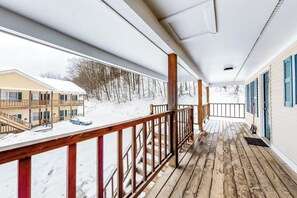 A covered wooden deck with a view of a building and snow-covered ground. - Slope-side condos with kitchenette & streaming (Ludlow)