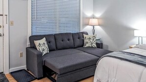 A modern room with a sofa bed, a bedside table with a lamp, and a door. - Slope-side condos with kitchenette & streaming (Ludlow)