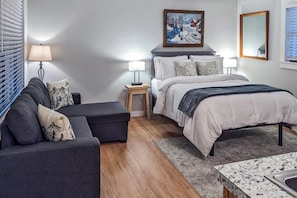 A bedroom with a bed, a sofa, a nightstand, a lamp, and a painting on the wall. - Slope-side condos with kitchenette & streaming (Ludlow)