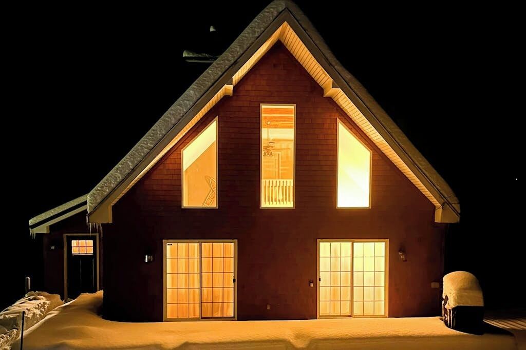A two-story wooden cabin with large windows and a snow-covered ground.