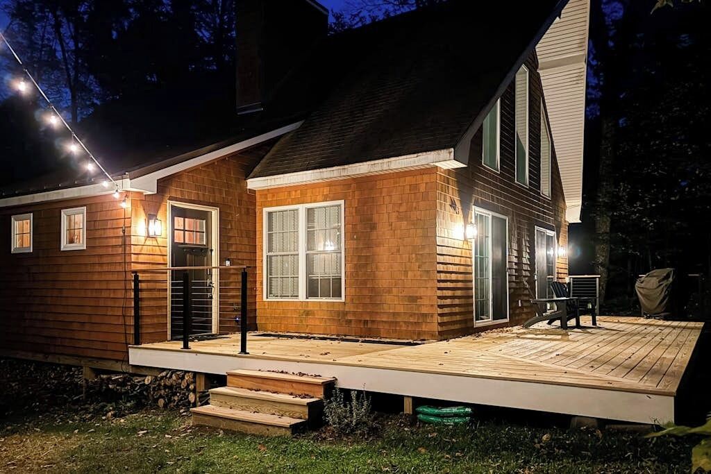 A two-story wooden house with a deck, a covered outdoor seating area, and string lights.