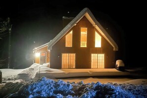 Eine zweistöckige Blockhütte mit verschneitem Einfahrt und gut beleuchtetem Eingang.