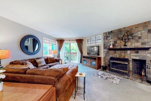 Ein Wohnzimmer mit Sofa, Fernseher, Kamin und Blick ins Freie.