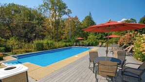 Una piscina con lettini e ombrelloni, circondata da alberi e un pontile in legno.