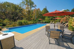 Ein Pool mit Liegestühlen und Sonnenschirmen, umgeben von Bäumen und einer Holzterrasse.