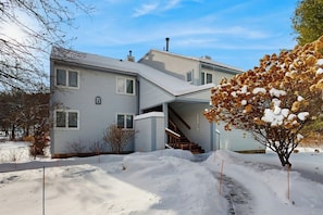 Ein zweistöckiges Haus mit einer Veranda, einer Treppe und einem schneebedeckten Garten.